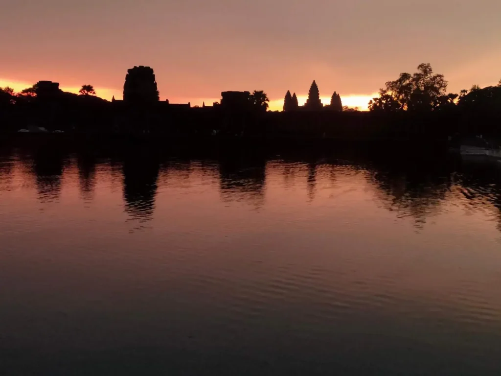 angkor-wat-amanecer-reflejo-lago-siem-reap.jpg Amanecer mágico en Angkor Wat, Camboya - El templo reflejado perfectamente en las aguas del lago al alba, con siluetas de turistas admirando el espectáculo y el cielo pintado en tonos dorados y rosados.